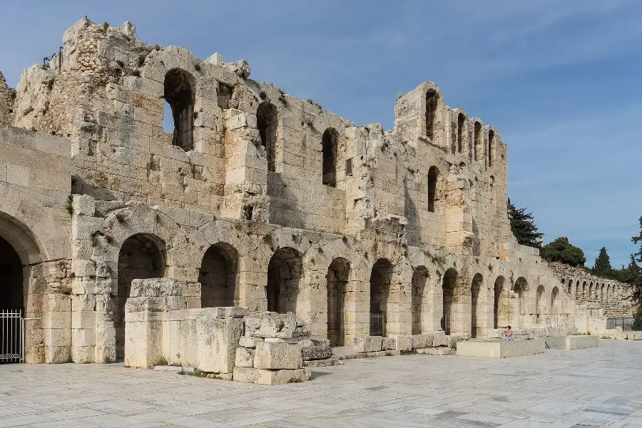 The arcaded stone stage wall of the Odeon of Herodes Atticus on the south slope of the Acropolis, seen from the paved walkway below under a clear blue sky