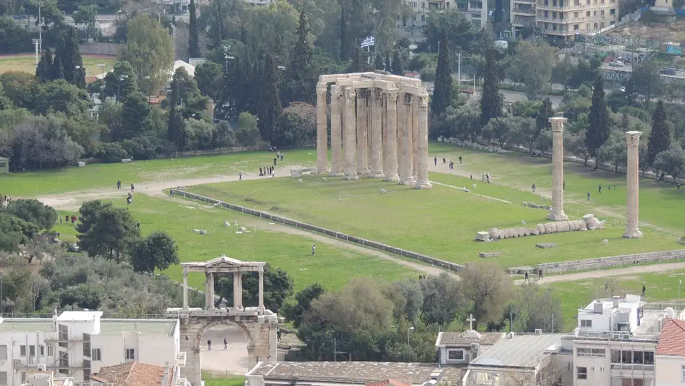 The standing columns of the Temple of Olympian Zeus on their green enclosure in central Athens, with the Arch of Hadrian and the city rooftops below