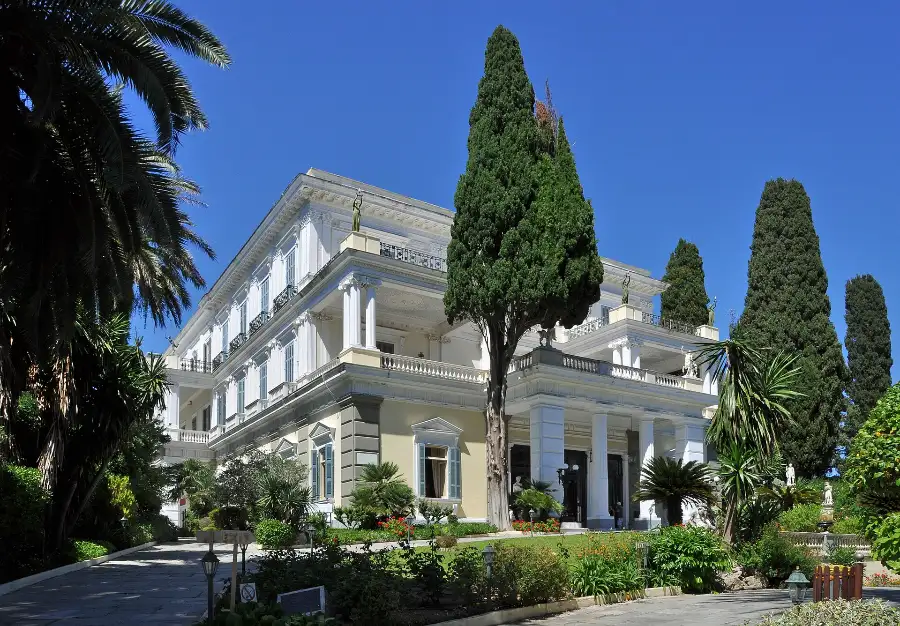 The Achilleion at Gastouri on Corfu: a white and ochre neoclassical palace with a colonnaded upper loggia and statues on the roofline, seen across its garden