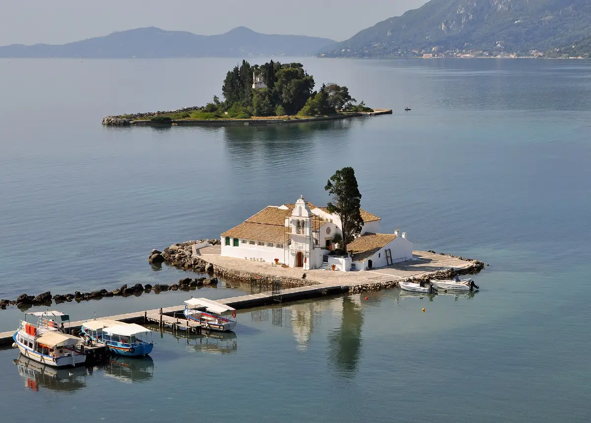 Vlacherna monastery on its small islet at Kanoni, Corfu, joined to the shore by a narrow causeway, with the wooded islet of Pontikonisi behind it