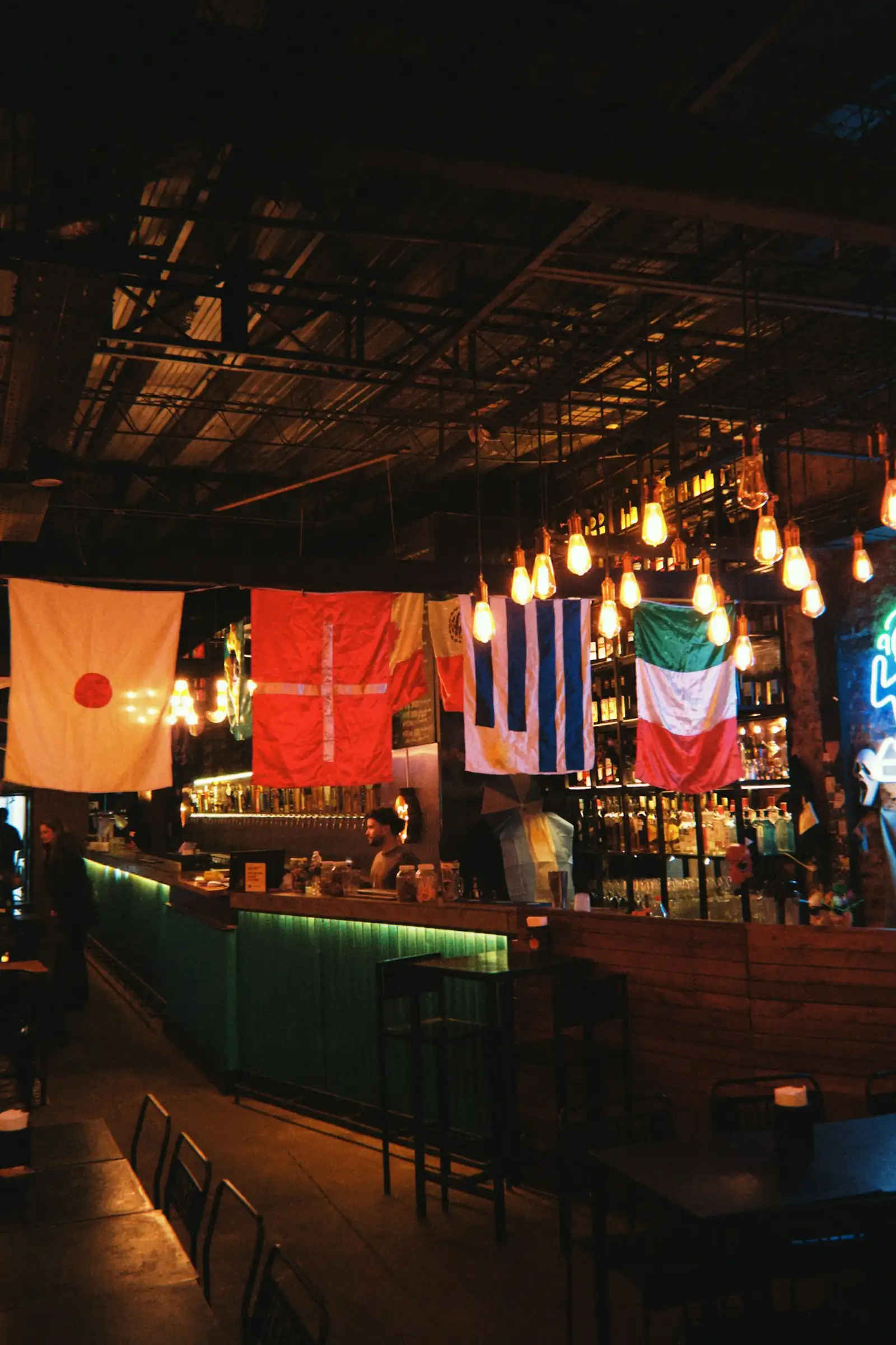 The interior of a dimly lit bar with national flags strung above the counter
