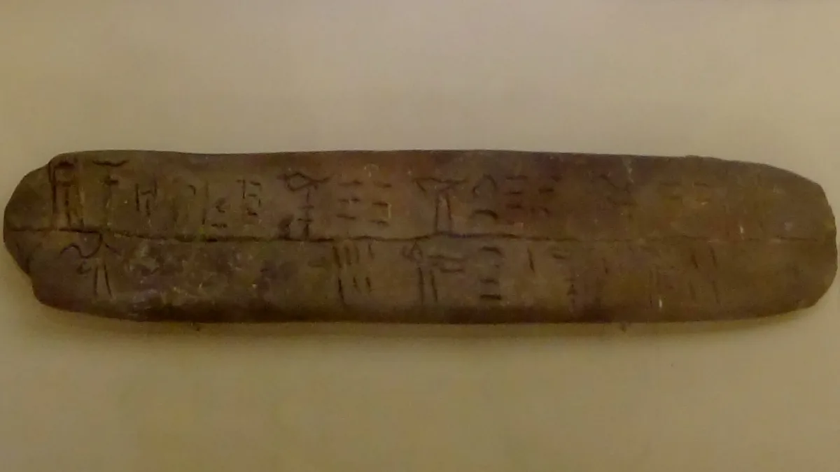 A long clay tablet incised with two lines of Linear B signs, displayed against a plain pale background in the Heraklion Archaeological Museum