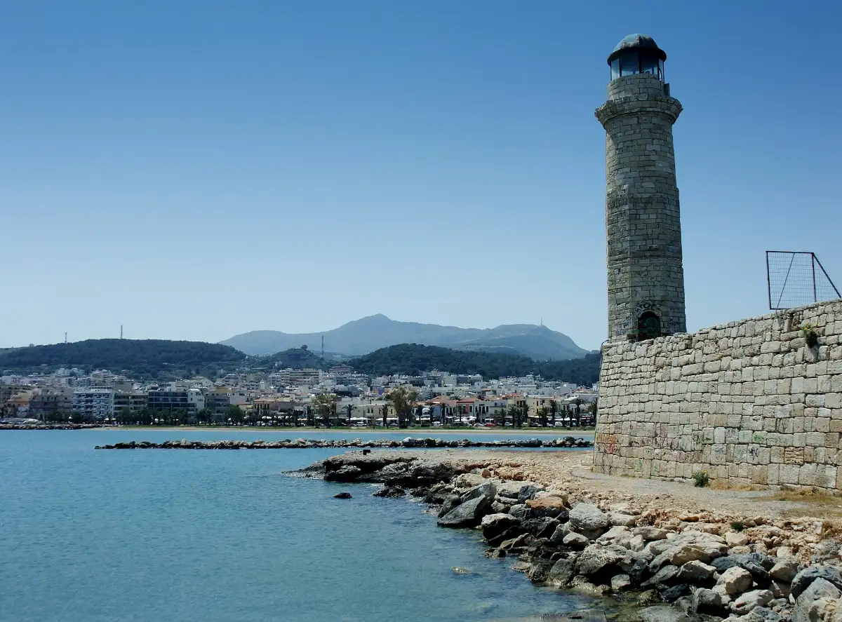 The stone lighthouse on the Venetian harbour wall at Rethymno, Crete, with the town beach and seafront curving away behind it