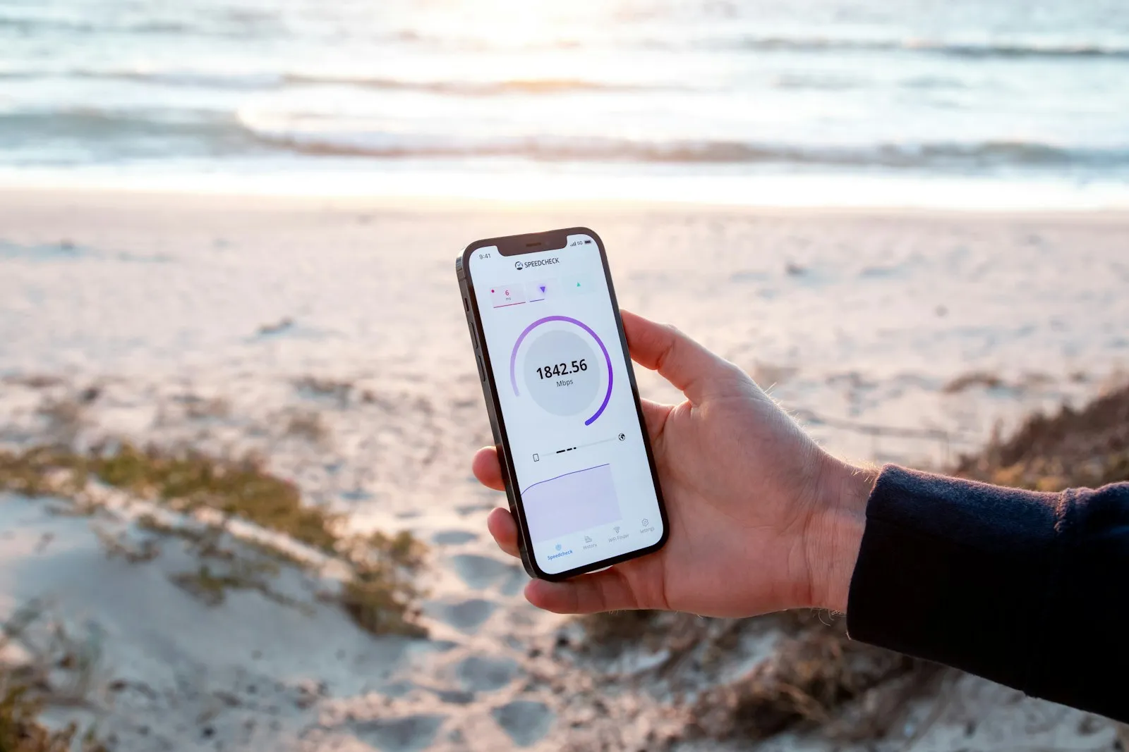 A hand holding a phone outdoors with a beach behind