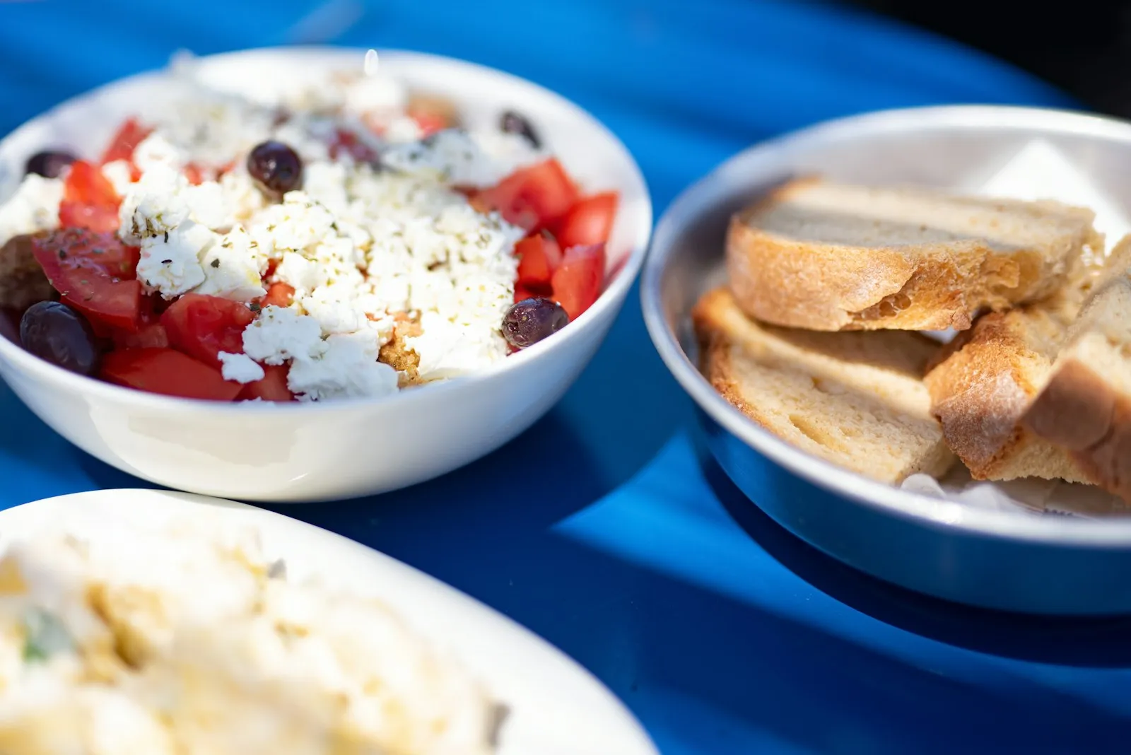 Bowls and small plates of food shared across a blue-painted table in Greece
