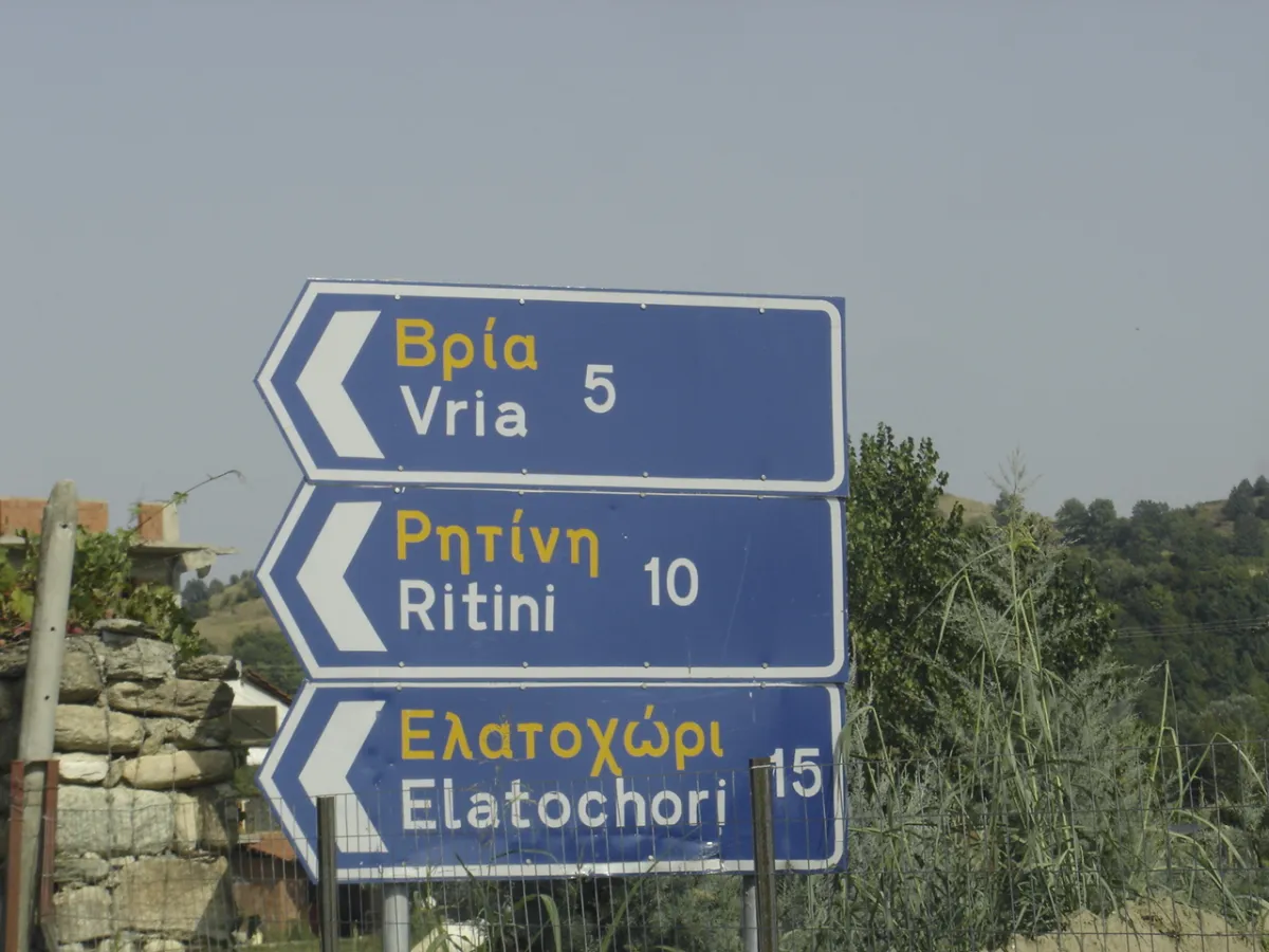 Greek road sign showing a place name in Greek capitals above its Latin-script transliteration