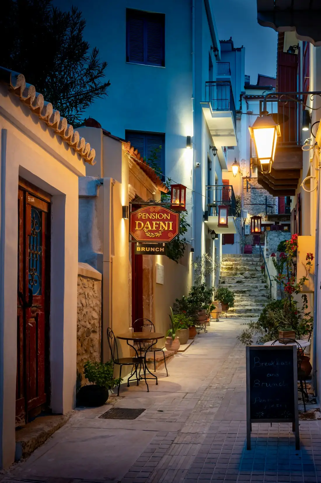 A narrow Greek street of lit buildings and steps at dusk