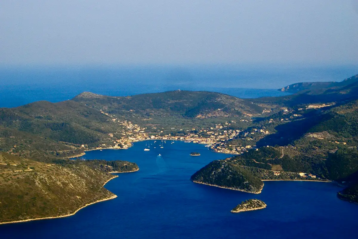 A view from high ground looking down over a deep bay almost completely ringed by green hills, with a small town spread along the far shore and the open sea hidden behind the headlands.