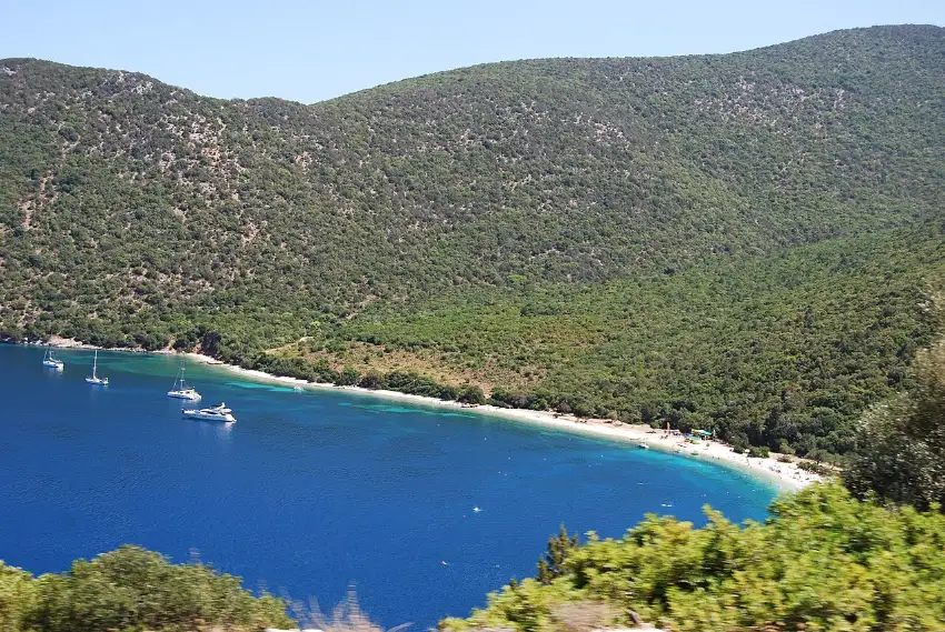 Antisamos beach on Kefalonia's east coast, a white-pebble bay backed by steep pine-wooded green hills, seen from above