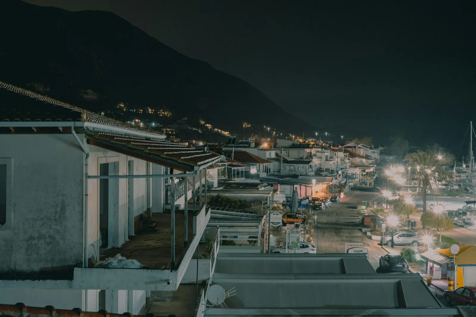 A lit Greek harbour at night with moored boats and a waterfront of tavernas