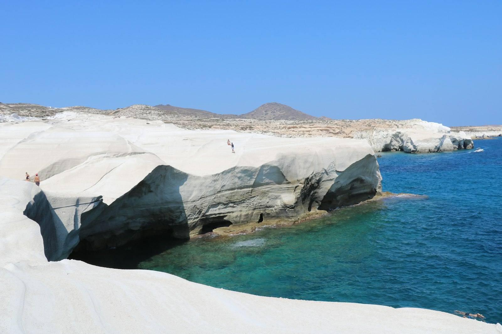 The white volcanic rock of Sarakiniko on Milos, wind-carved into pale folds beside a turquoise inlet.