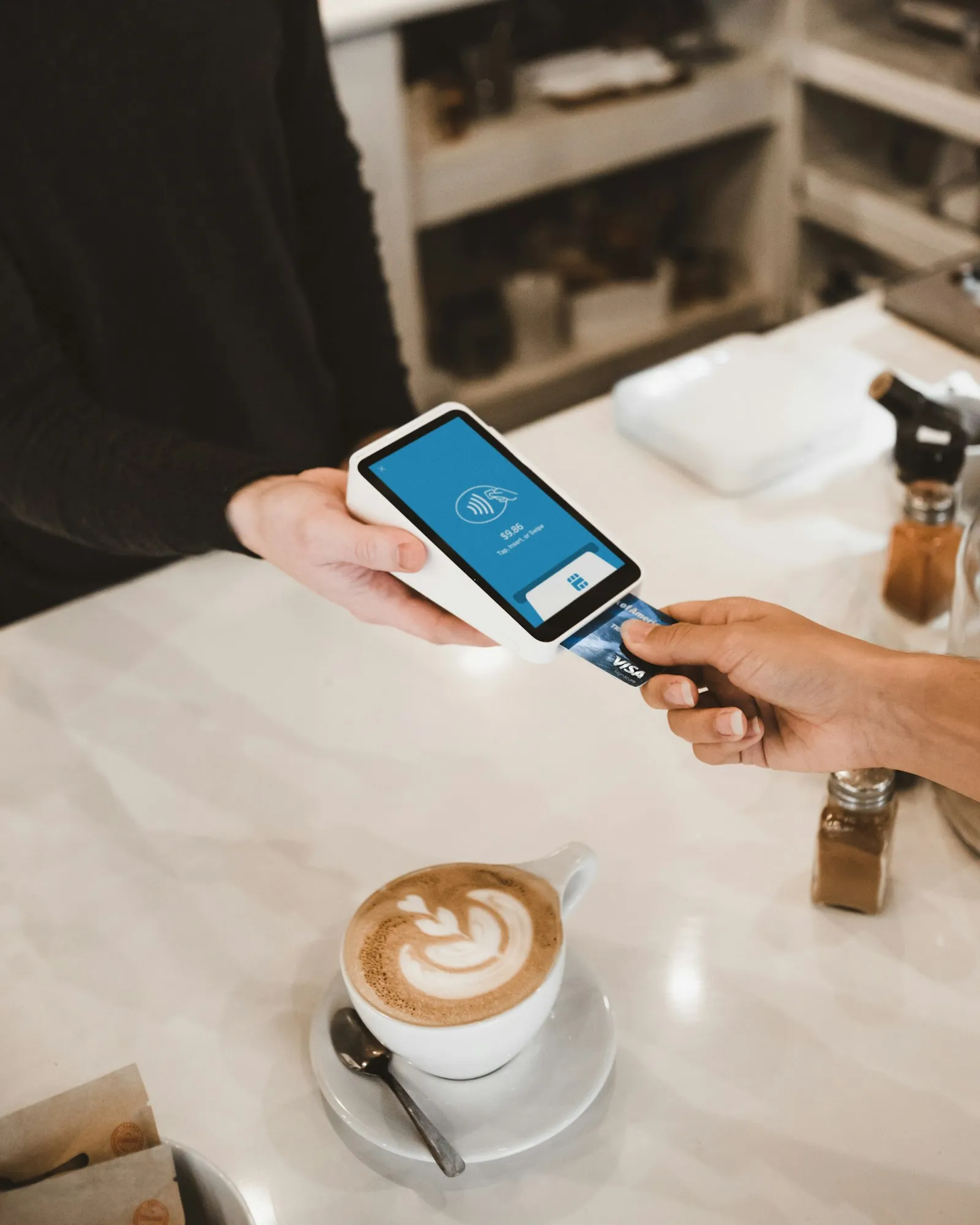 A hand holding a payment card against a card terminal