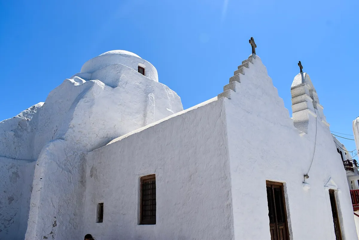 The white sculpted church of Panagia Paraportiani in Mykonos Town, its rounded whitewashed forms against a blue sky