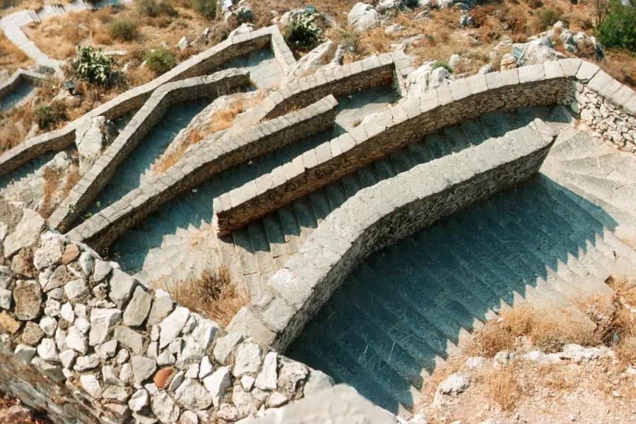 A long stone staircase zig-zagging up a steep, bare hillside toward fortress walls at the top, with no shade along its length.
