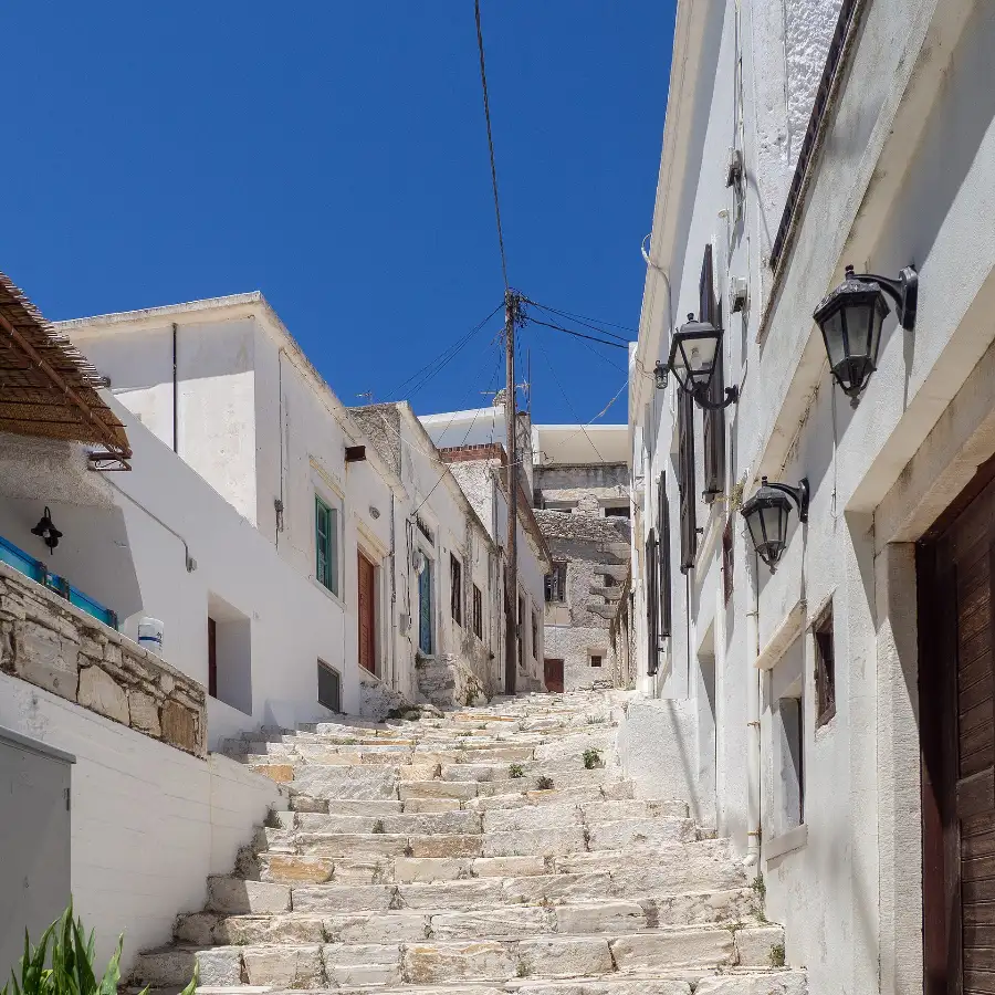 A stepped lane in Apeiranthos on Naxos paved with irregular slabs of pale marble, climbing between whitewashed houses and iron lanterns under a deep blue sky