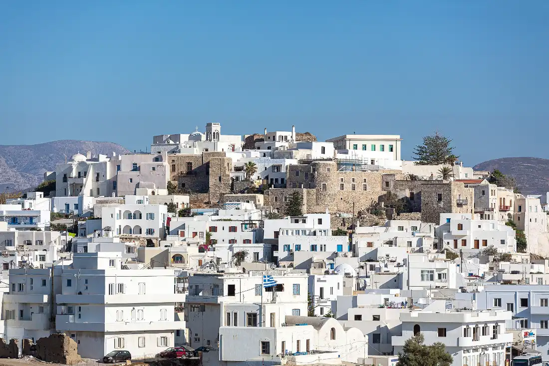 Naxos Town seen from across the water, white houses stacked up a hill below the old stone Kastro