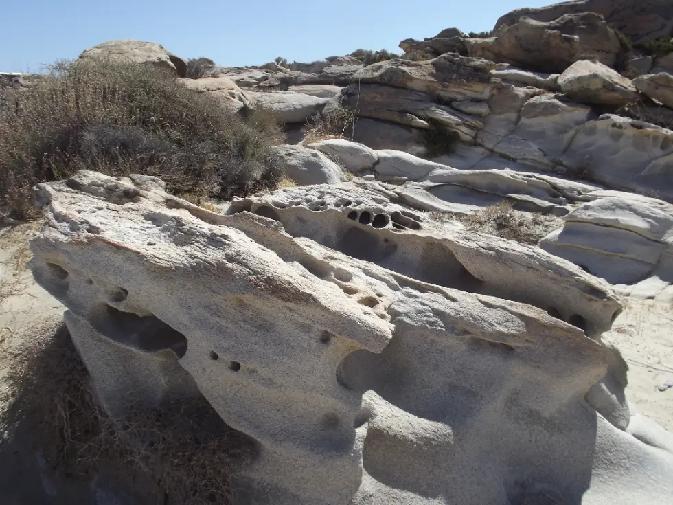 The sculpted golden rock formations at Kolymbithres beach on Paros, smooth weathered boulders around pockets of pale sand and clear water