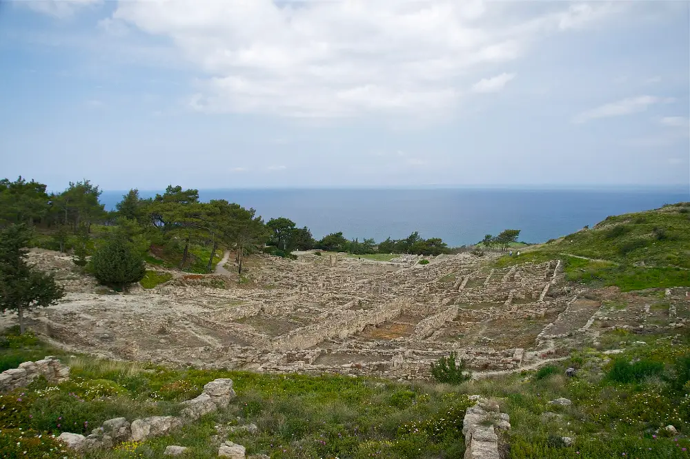 The excavated terraces of ancient Kameiros on Rhodes: grids of low pale stone walls stepping down a green hillside towards an open sea