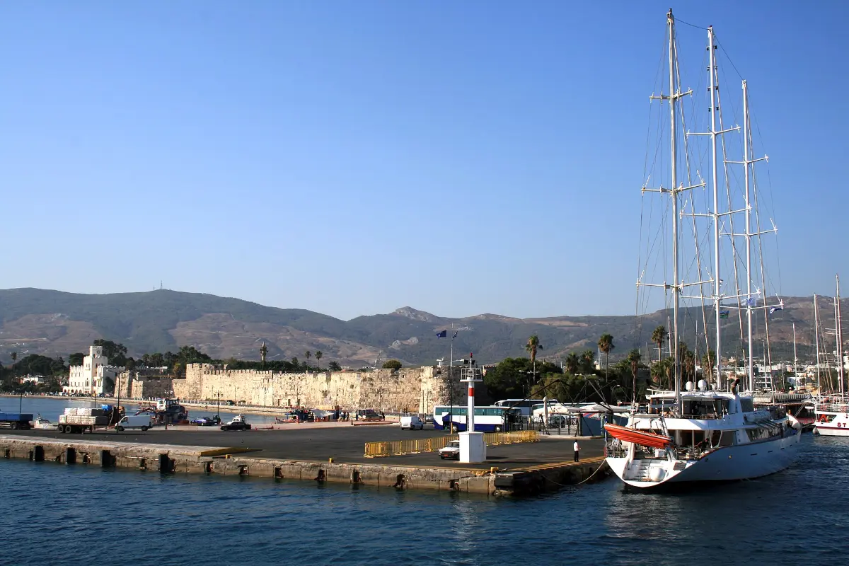 The low crenellated walls of the Neratzia castle along the waterfront at Kos town, seen from the sea, with a ferry quay and a moored schooner in front