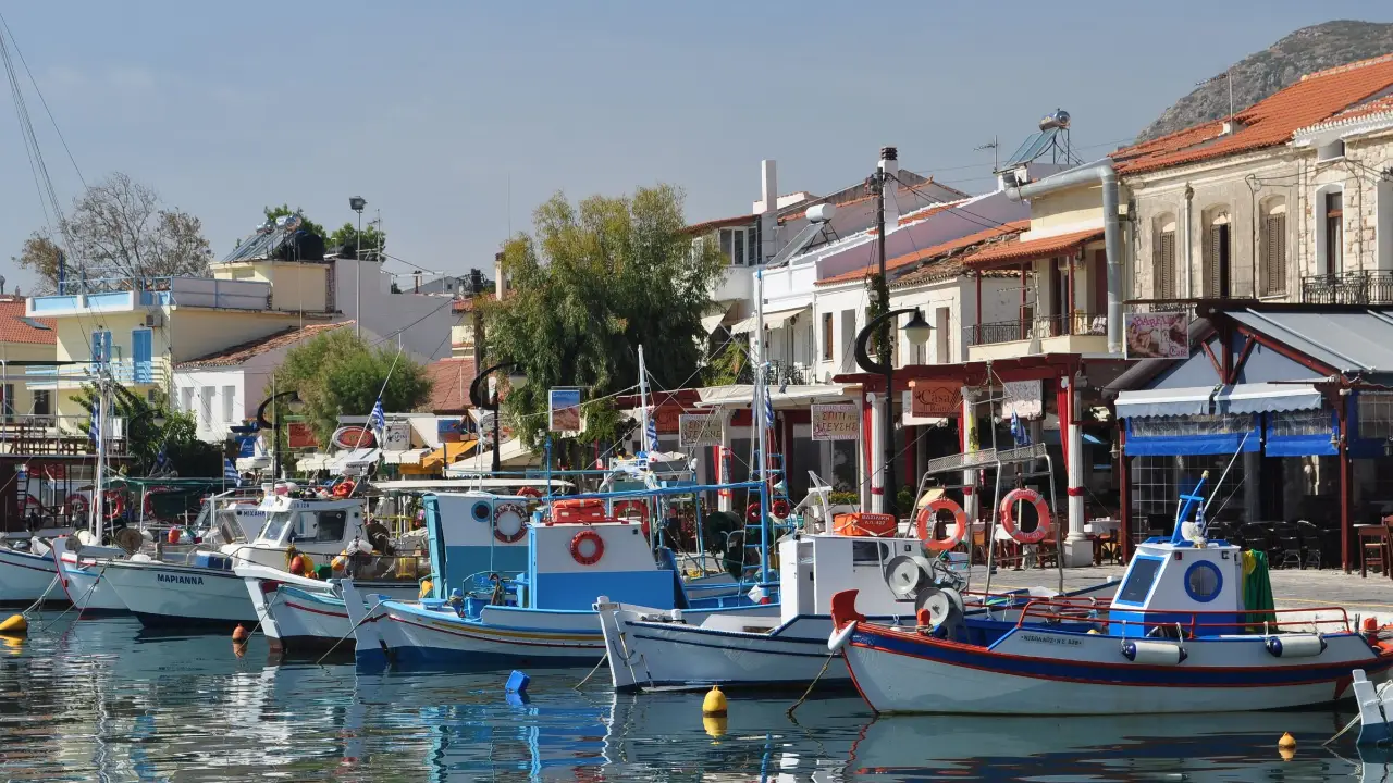 Fishing boats moored along the dock at Pythagorio harbour on Samos, the low waterfront buildings of the town behind them and calm water holding their reflection