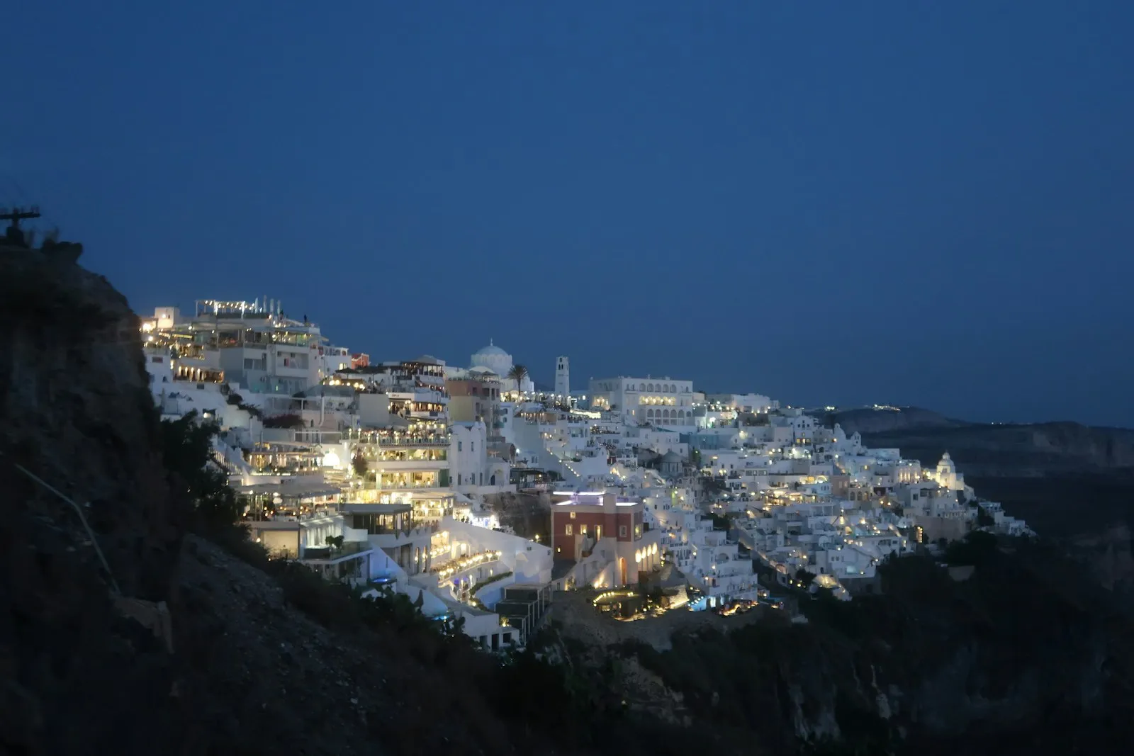 Whitewashed Santorini buildings lit on a hillside at blue hour, quiet and empty