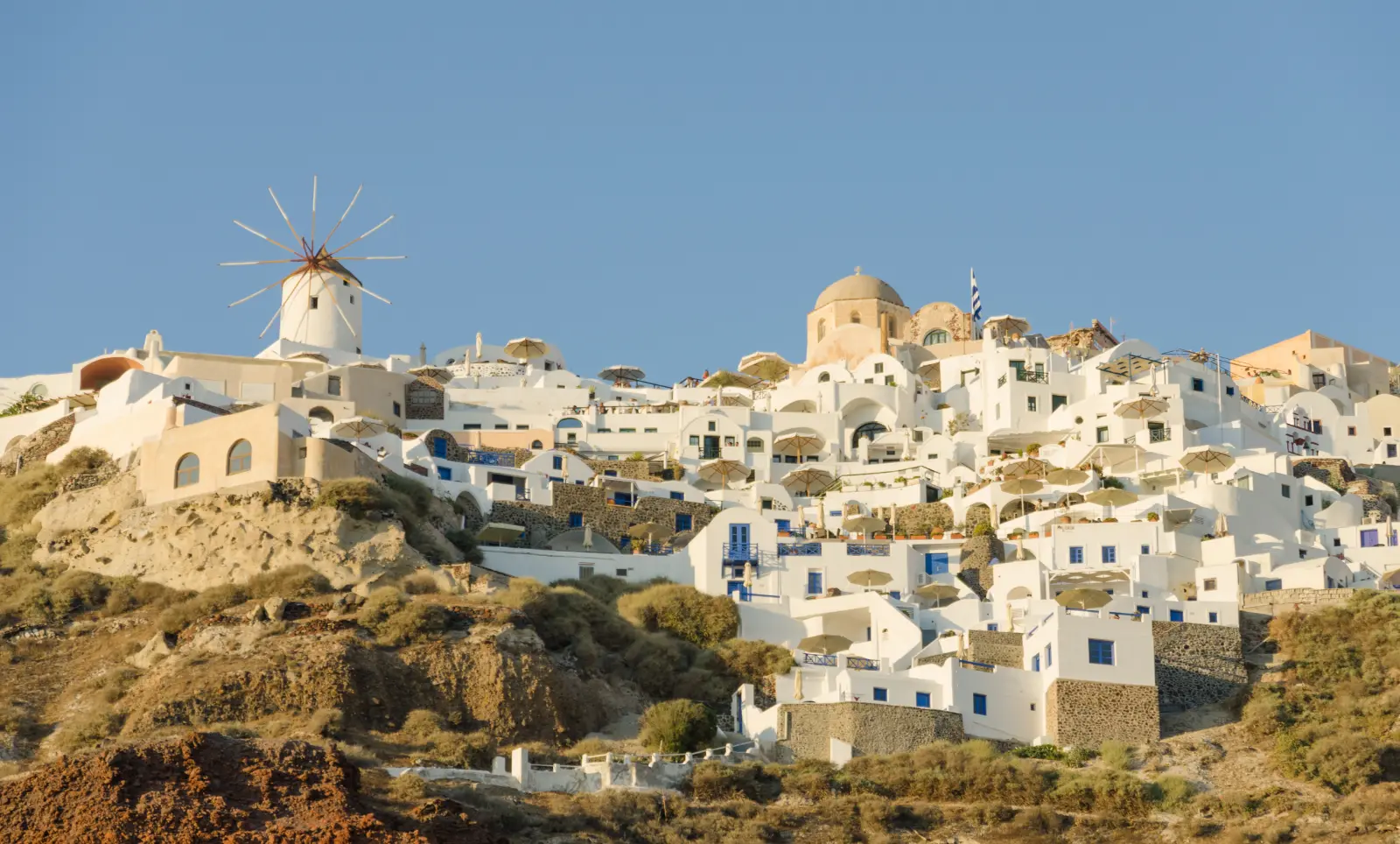The white terraced town of Oia stepping down the dark caldera cliff of Santorini, seen from the water