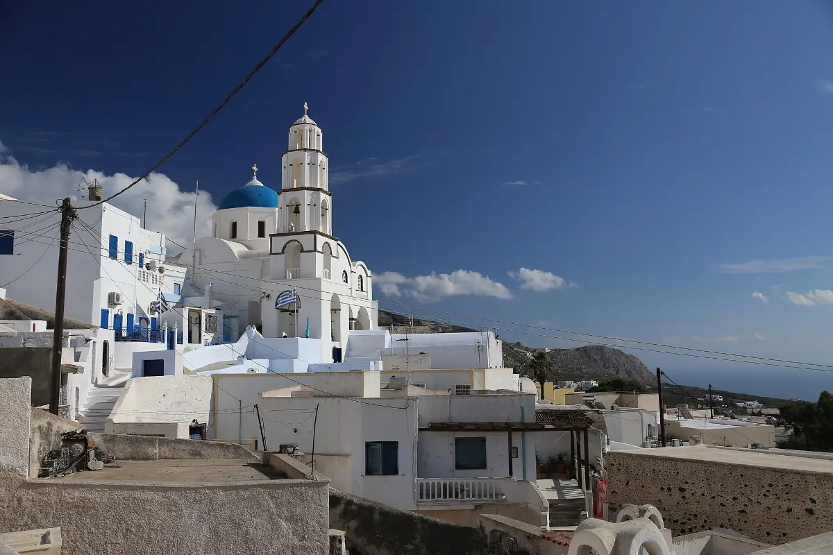 The blue-domed church and bell tower of Pyrgos standing above whitewashed houses on the hillside, inland Santorini