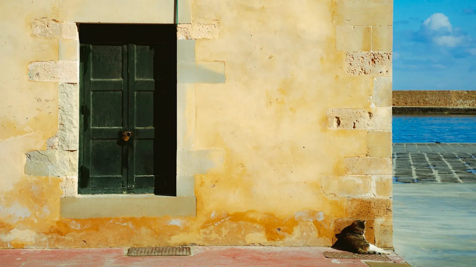 A closed green door in a weathered sunlit wall in Chania, Crete
