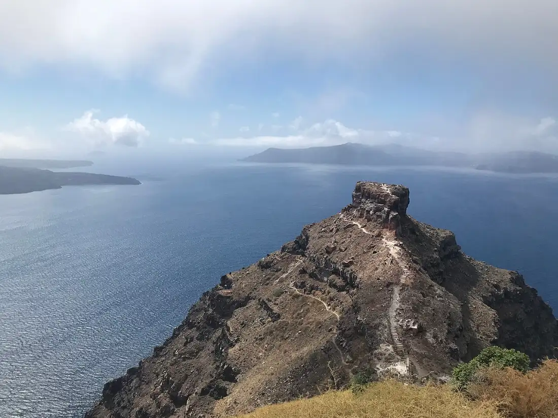 Skaros Rock seen from the Imerovigli rim, Santorini, the caldera sea beyond and a stepped path climbing its spine