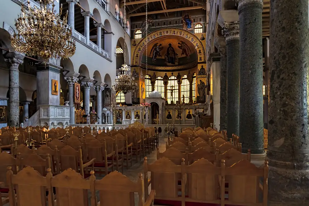 Inside Agios Dimitrios in Thessaloniki: rows of green marble columns carrying arcades down an empty nave, brass chandeliers overhead and a gold mosaic in the apse