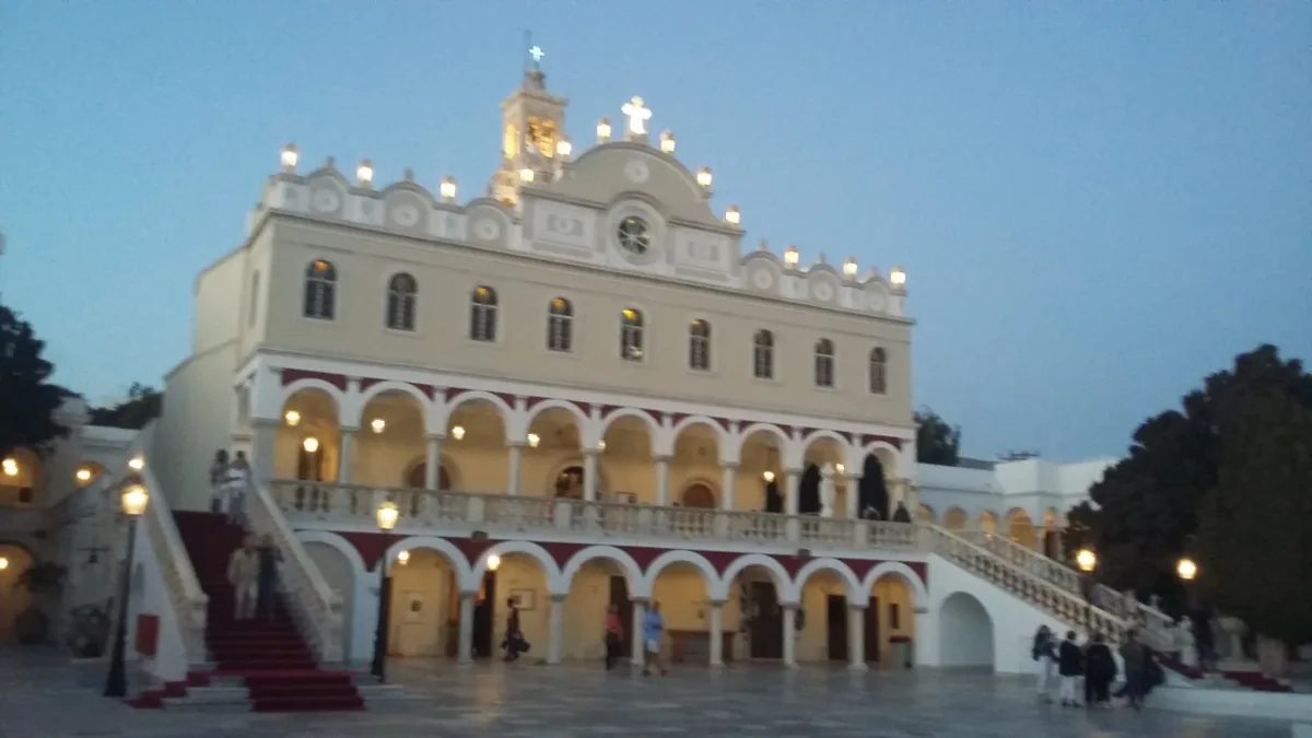 A large white church lit at dusk, its front made up of two tiers of arcades under a bell tower, with a broad marble staircase in front of it and a red carpet runner laid down the middle of the steps.