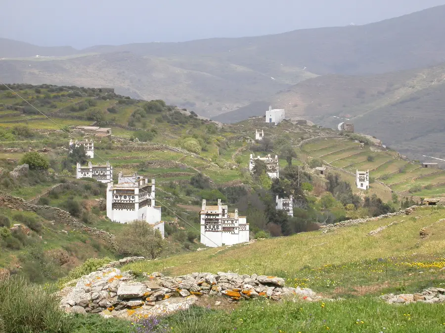 Half a dozen white two-storey stone towers scattered across a green terraced valley, each with its upper floor pierced by dense geometric patterns of small openings.