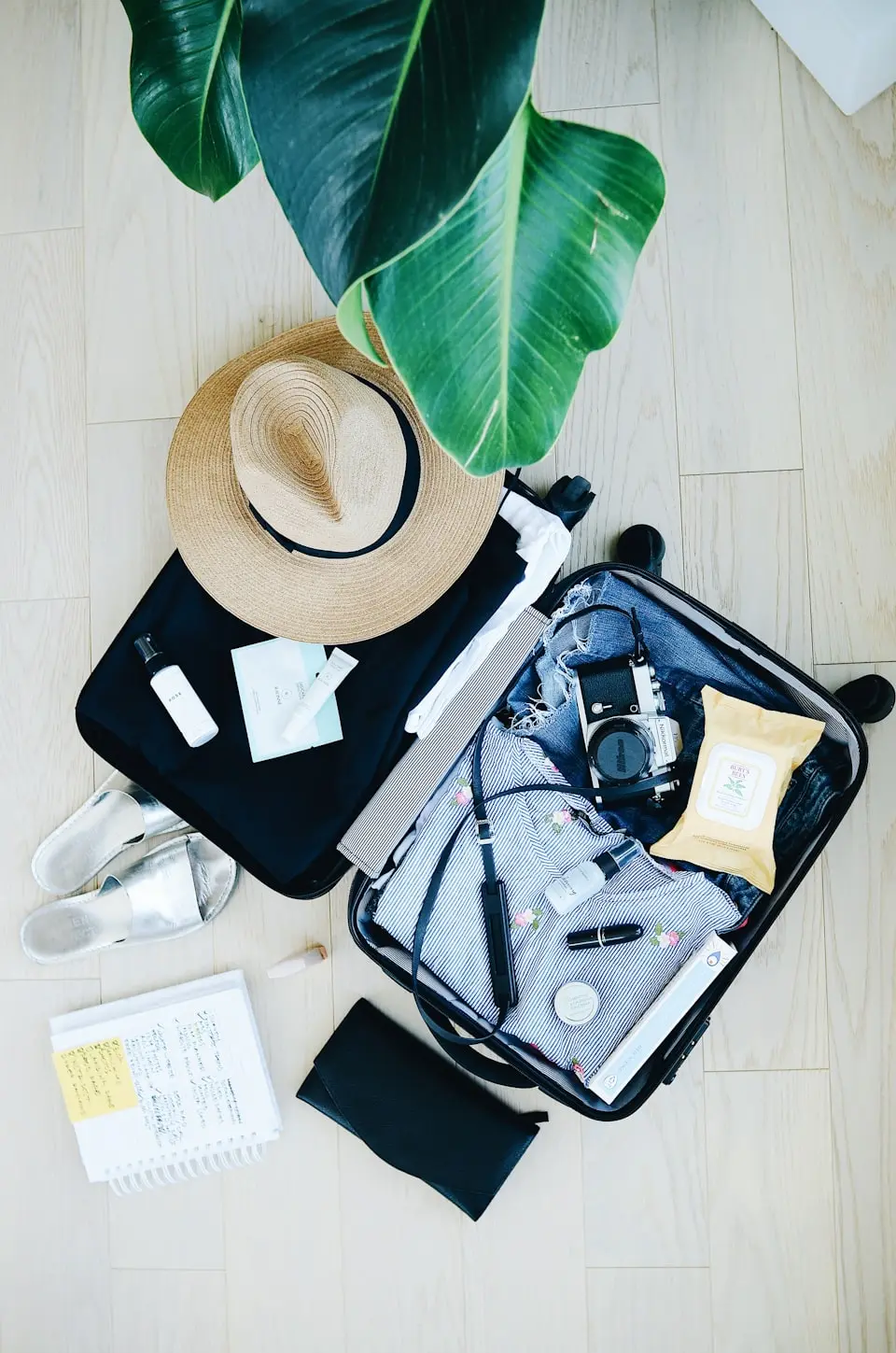 An open suitcase packed with travel essentials and a sun hat