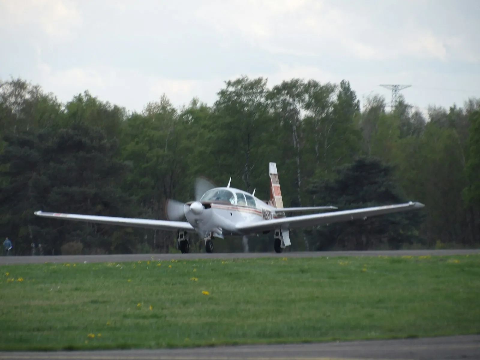 A small propeller aircraft on a runway with trees behind