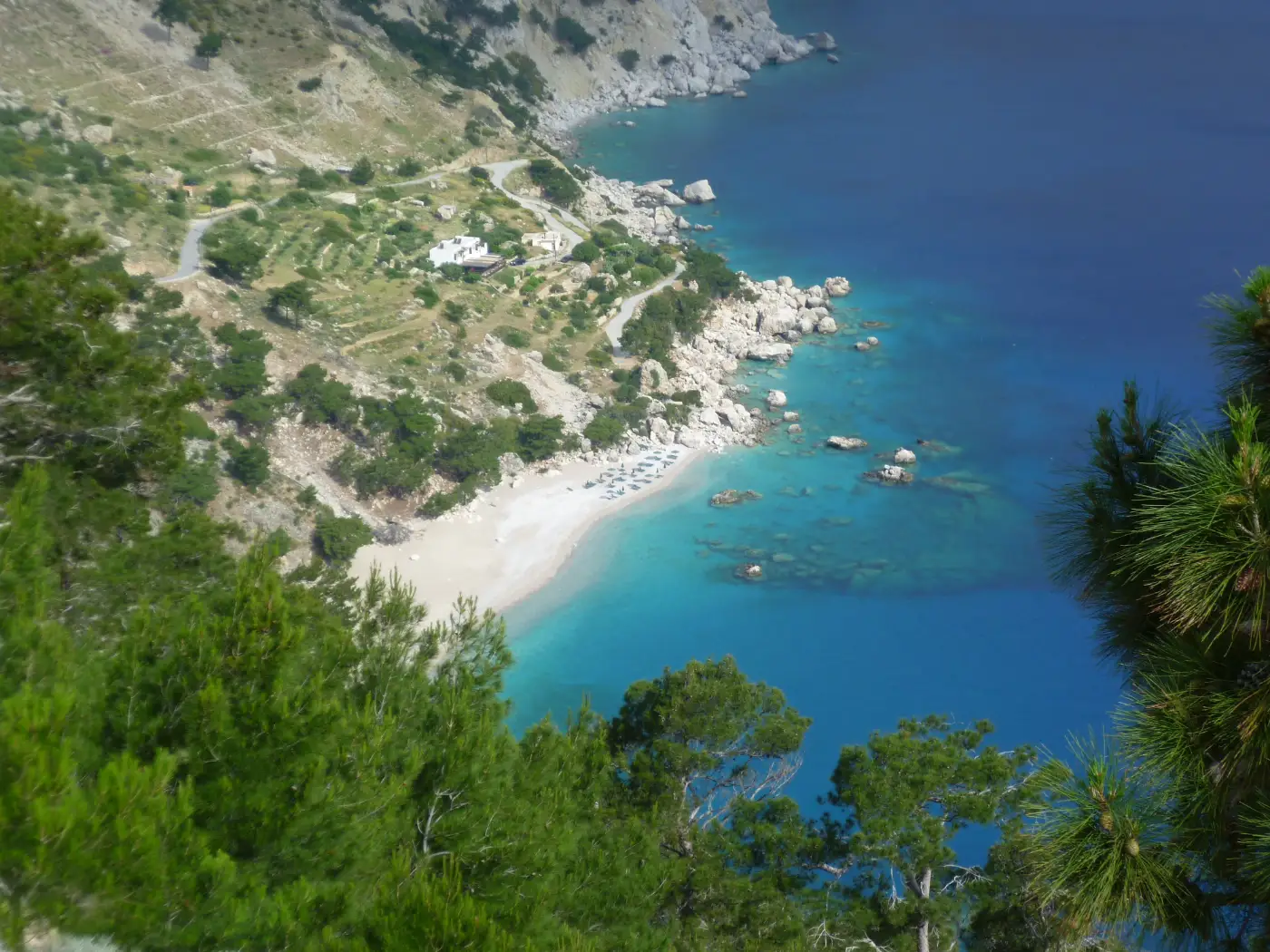 Apella beach on Karpathos seen from the road above, pale shingle in a green cove